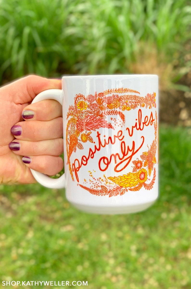 May include: White ceramic mug with a floral design in shades of orange and yellow. The mug has the text "positive vibes only" written in red cursive.