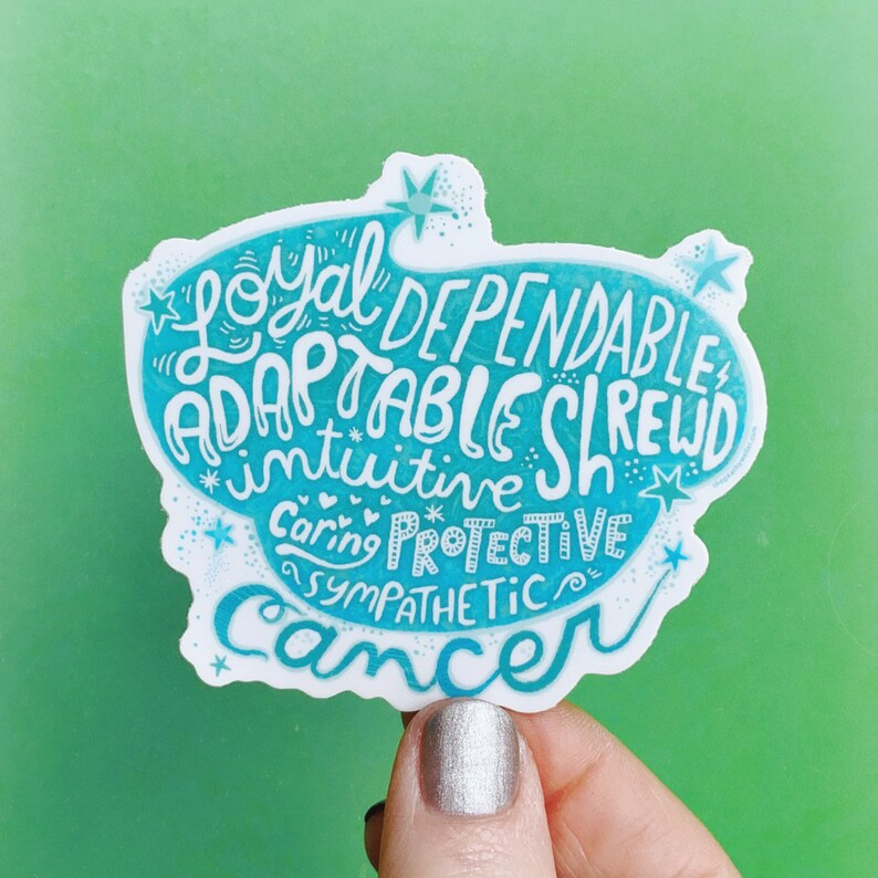 May include: A white sticker with a teal blue border and text. The sticker features the word "Cancer" in cursive, along with words like "Loyal," "Dependable," and "Adaptable." The background is a solid green.