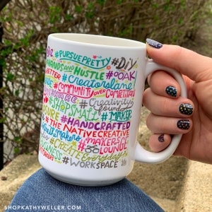 May include: White ceramic mug with a colourful design featuring the words "#PURSUE PRETTY #DIY #HANDS AND HUSTLE #OOAK #CREATORSLANE #COMMUNITUOVER COMPETITION #SHARE #CREATIVITY #SHOPSMALL #MAKER #HANDCRAFTED #THE NATIVECREATIVE #MAKERS #MAKERSLOUNGE #CREATE EVERYDAY #WORKSPACE"