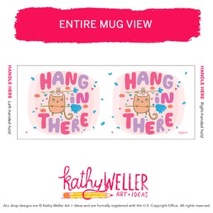 May include: White ceramic mug with a pink background and a cartoon cat holding a stick with a blue flower on it. The text "Hang in there" is written in purple and pink letters.