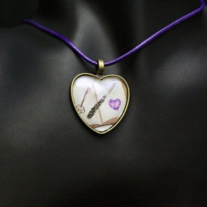 Libro abierto con una llave, un abrecartas y un corazón morado de cristal en un colgante de cabujón en forma de corazón en un cordón morado de 18"