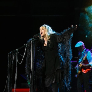 Stevie Nicks in hand knit black shawl by Crickets Knits designer Celeste Meyeres. Dark stage concert lighting.