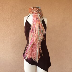 May include: A long, flowing scarf with a mix of pink, brown, and blue yarn. The scarf is draped over a brown dress form.