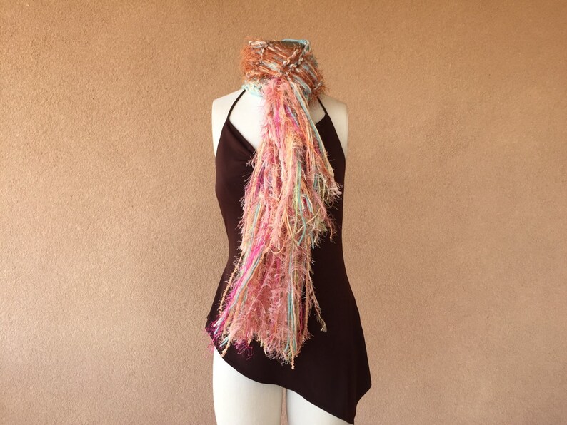 May include: A long, flowing scarf with a mix of pink, brown, and blue yarn. The scarf is draped over a brown dress form.