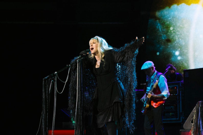 Stevie Nicks in hand knit black shawl by Crickets Knits designer Celeste Meyeres. Dark stage concert lighting.