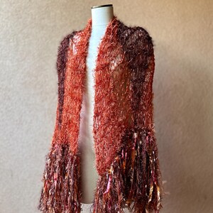 May include: A long, fuzzy shawl with a gradient of brown and orange colors. The shawl has long, fringed edges.