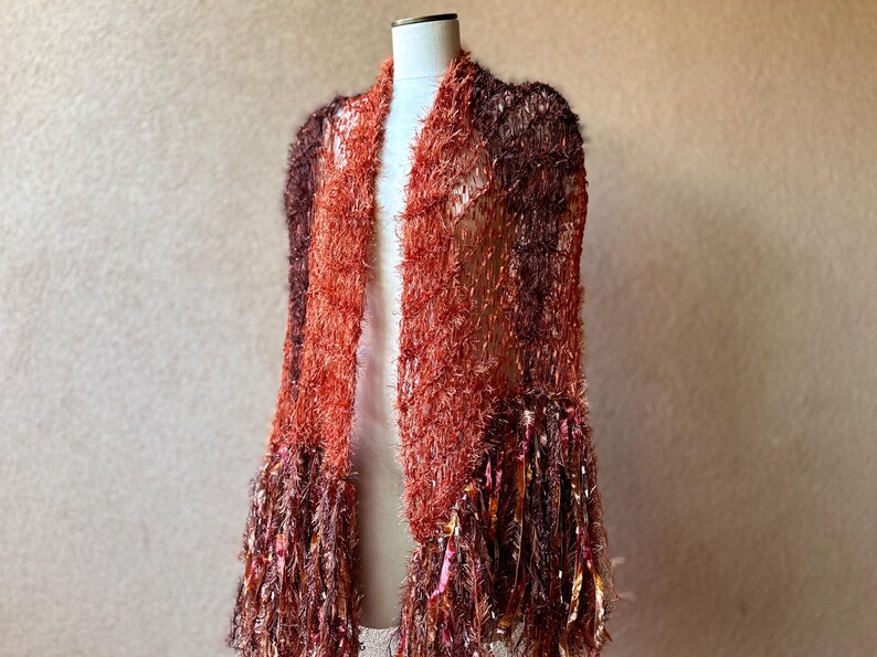 May include: A long, fuzzy shawl with a gradient of brown and orange colors. The shawl has long, fringed edges.