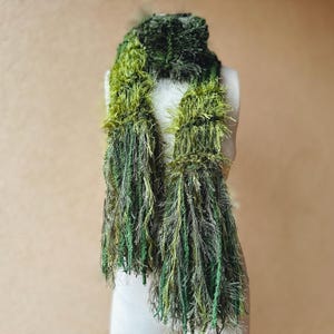 May include: A green and brown fuzzy scarf with long fringe. The scarf is made of a soft, textured yarn.