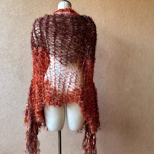 May include: A brown and orange crochet shawl with a fringe border. The shawl is draped over a mannequin.