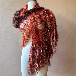 May include: A brown and orange fuzzy shawl with long fringe. The shawl is draped over a white mannequin.