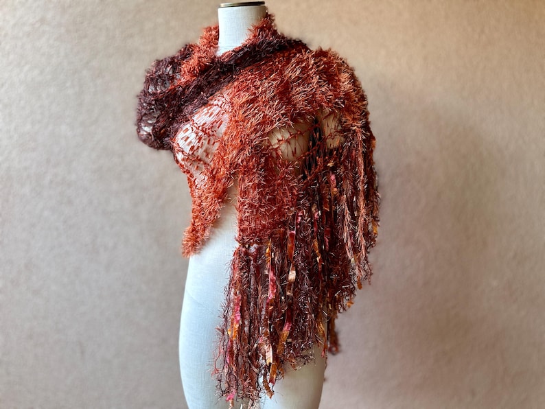 May include: A brown and orange fuzzy shawl with long fringe. The shawl is draped over a white mannequin.