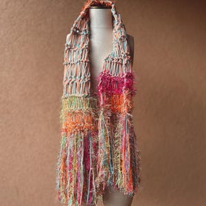 May include: A colorful crocheted scarf with a fringe. The scarf is made with a variety of colors, including pink, orange, green, and blue.