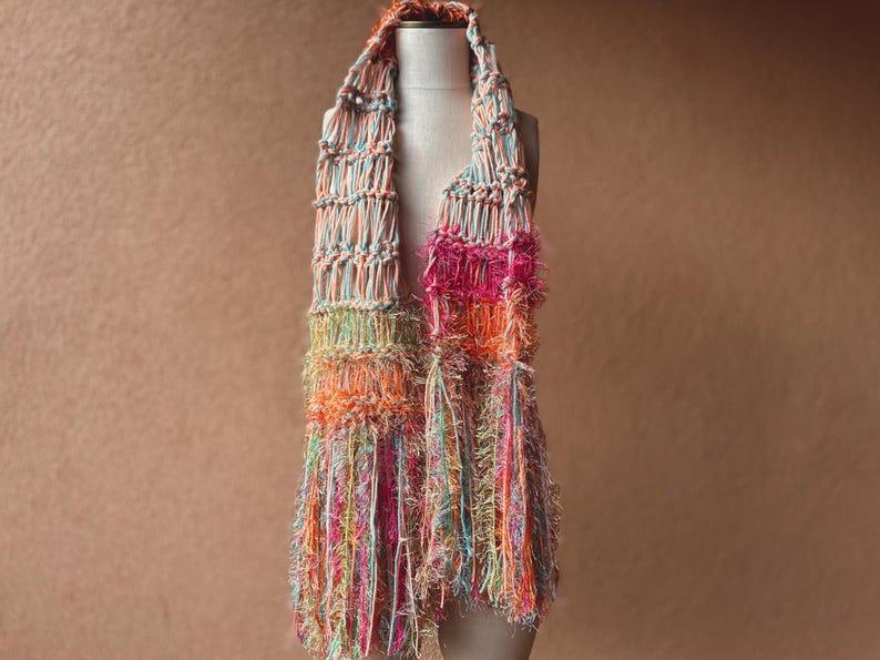 May include: A colorful crocheted scarf with a fringe. The scarf is made with a variety of colors, including pink, orange, green, and blue.