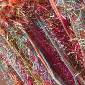 May include: Close-up of a colorful yarn with a variety of textures and colors, including orange, pink, blue, and green.