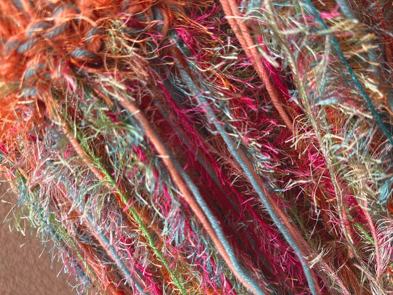 May include: Close-up of a colorful yarn with a variety of textures and colors, including orange, pink, blue, and green.