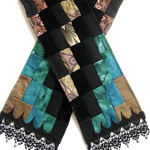 May include: A patchwork scarf with a variety of patterned squares in black, brown, teal, and floral designs. The scarf has a black lace trim along the bottom edges and a leopard print section at the top. The word "KAMBRIEL" is at the bottom.