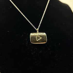 May include: A gold necklace with a pendant shaped like the YouTube play button.