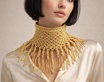 May include: A golden-yellow crochet collar with a high neck and fringe detail. The collar is made of a textured yarn and has a delicate, open weave design. The fringe hangs down from the bottom edge of the collar.