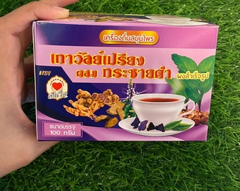 May include: A purple box with a picture of a cup of tea and a variety of herbs. The box is labeled "เครื่องดื่มสมุนไพร เถาวัลย์เปรียง ผสม กระชายดำ ผงสำเร็จรูป" and "ขนาดบรรจุ 100 กรัม".