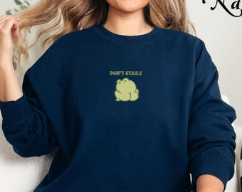 May include: A navy blue sweatshirt with a green frog graphic and the text "Don't Stare" in white.