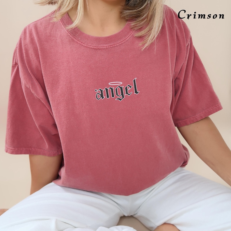 May include: A crimson red t-shirt with a black graphic of the word "angel" with a halo above it.