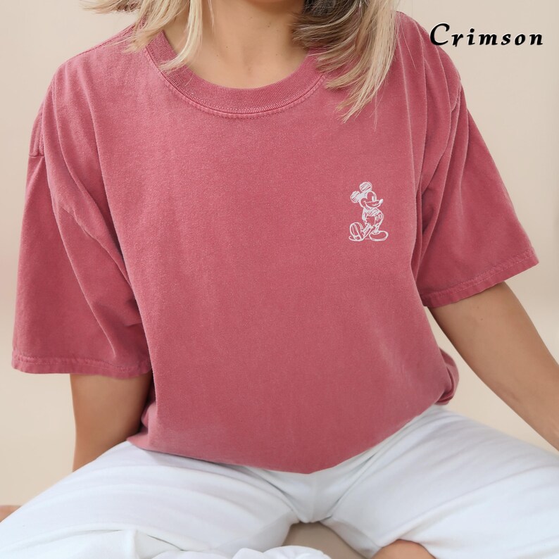 May include: A crimson red t-shirt with a white embroidered Mickey Mouse graphic. The t-shirt has a relaxed fit and short sleeves.
