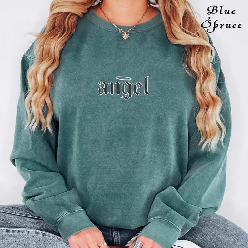 Pode incluir: Uma camisa de moletom verde com um gr&aacute;fico preto da palavra "angel" com uma aur&eacute;ola acima.
