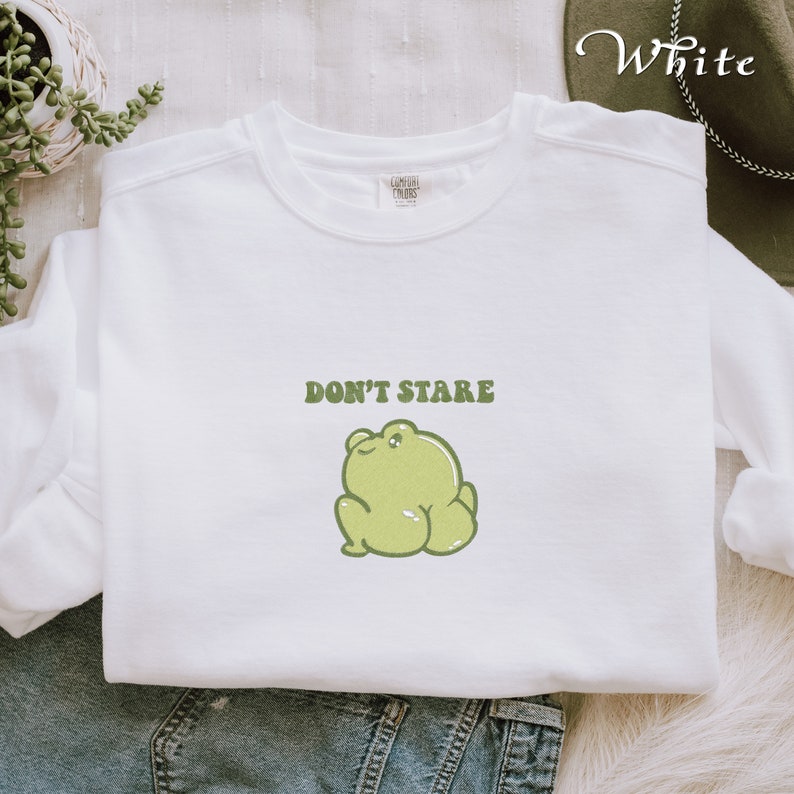 May include: White sweatshirt with a green frog illustration and the text "DON'T STARE" in green.