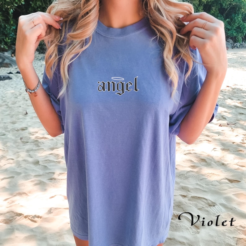 May include: A light blue t-shirt with the word "angel" printed in black with a halo above the word. The t-shirt is oversized and has a relaxed fit.