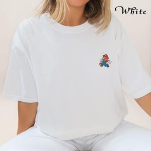 May include: White t-shirt with a small embroidered image of Mario, a video game character, on the left chest.