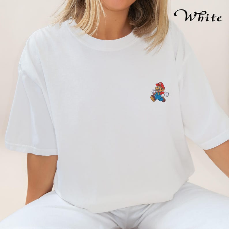 May include: White t-shirt with a small embroidered image of Mario, a video game character, on the left chest.