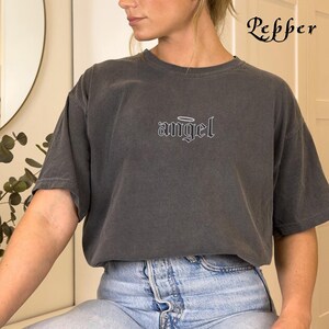 May include: A dark gray t-shirt with the word "angel" in white lettering with a halo above it.