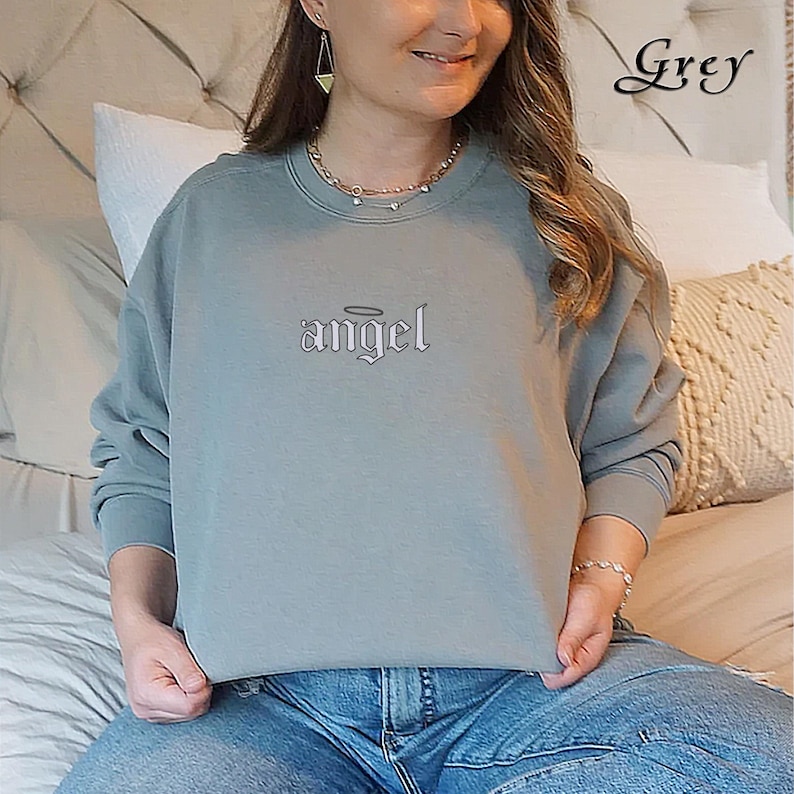 Pode incluir: Uma camisa de moletom cinza com a palavra "angel" em fonte g&oacute;tica com uma aur&eacute;ola acima.