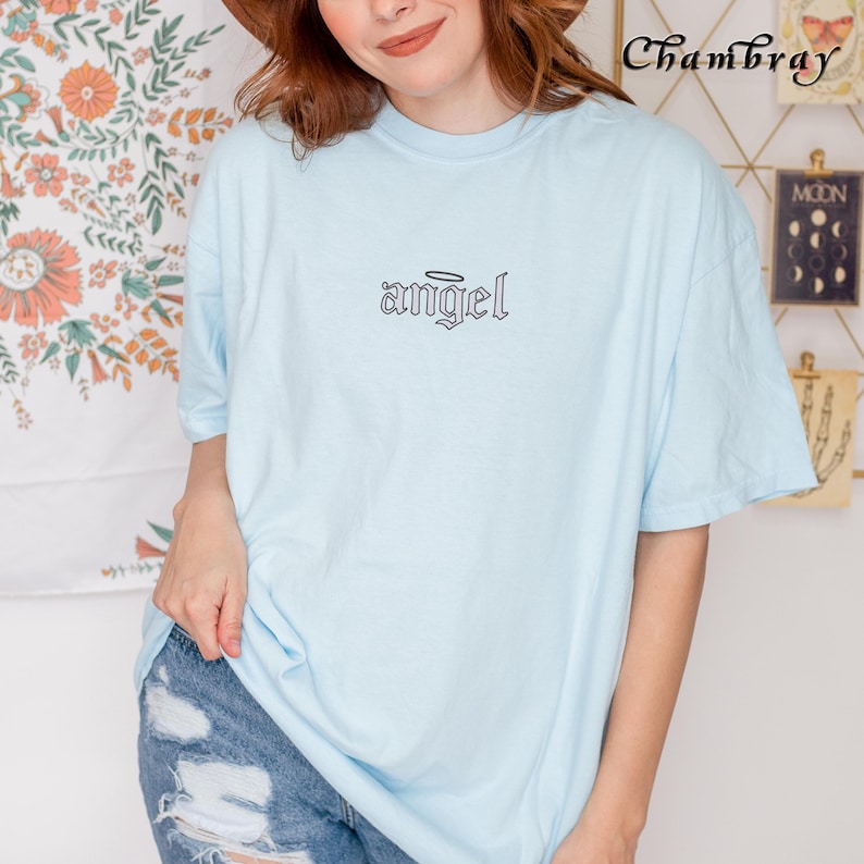 May include: A light blue t-shirt with a black graphic of the word "angel" in a gothic font with a halo above it.