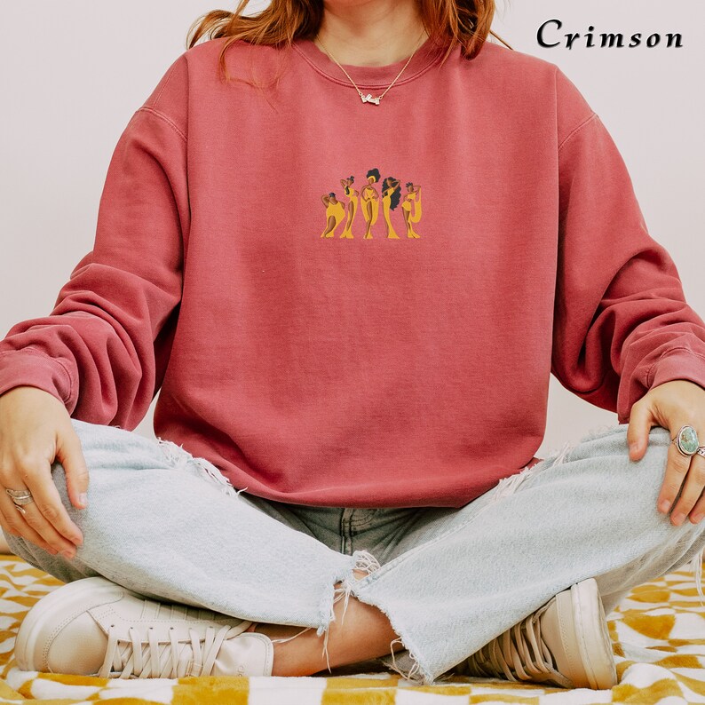 Op de afbeelding: Een crimson sweatshirt met een afbeelding van vijf vrouwen in gele jurken. De vrouwen staan in een rij en hebben donker haar.