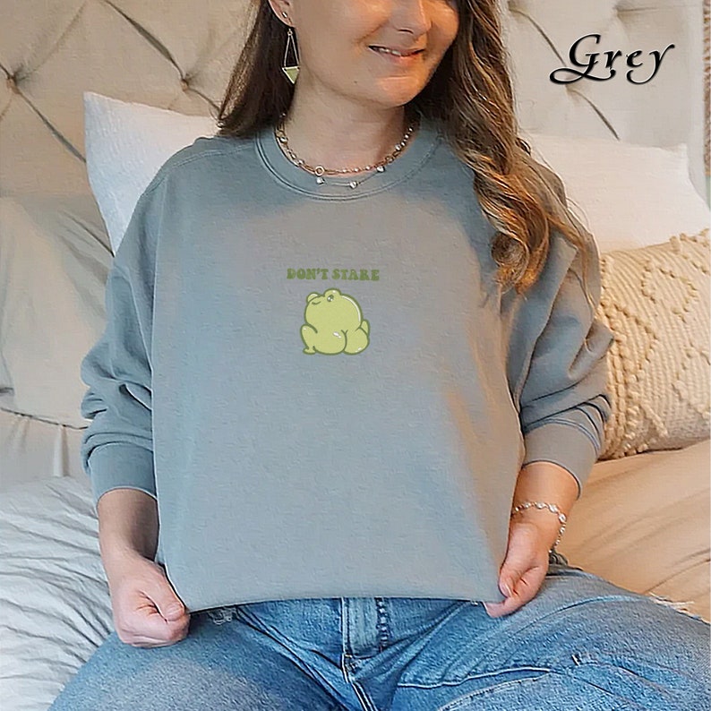 May include: A grey sweatshirt with a green frog graphic and the text "Don't Stare" printed on the front.