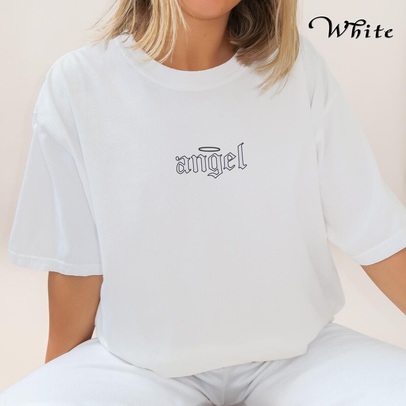 May include: White t-shirt with a black graphic of the word "angel" with a halo above it.