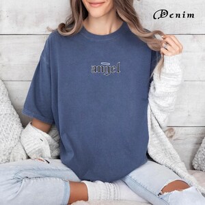 May include: A woman wearing a dark blue t-shirt with the word "angel" in a gothic font with a halo above it.