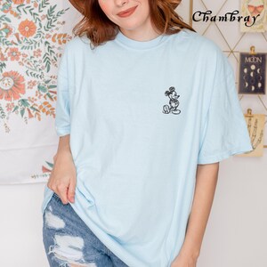 May include: A light blue t-shirt with a black and white embroidered image of Mickey Mouse on the left chest.