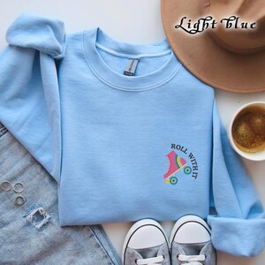 May include: Light blue sweatshirt with a pink roller skate graphic and the text "Roll With It".