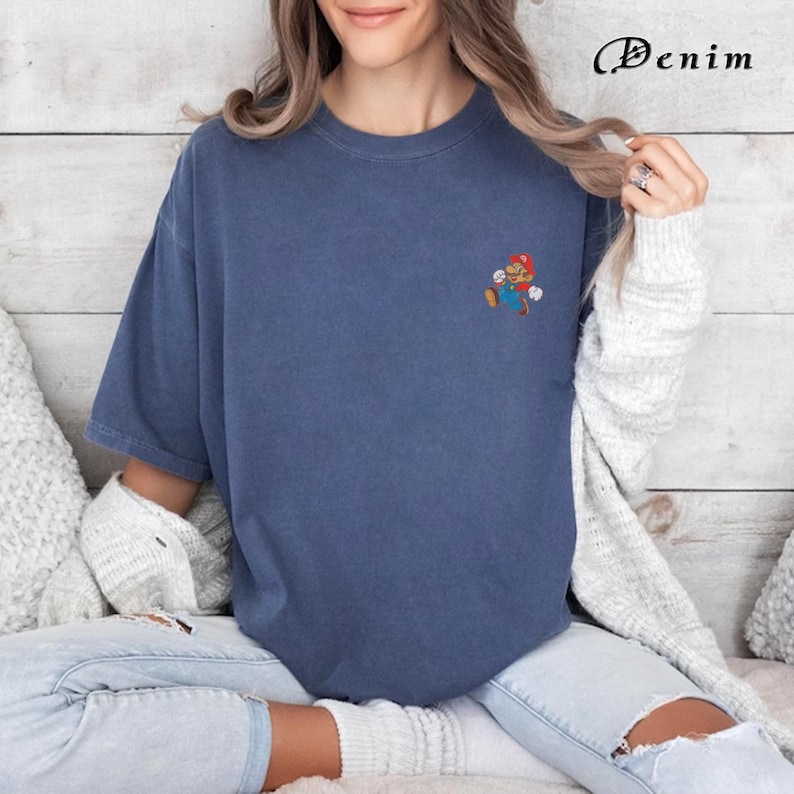 May include: A blue t-shirt with a small embroidered image of a video game character on the left chest. The character is red and white and is running.