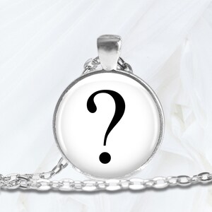 May include: A silver chain necklace with a round pendant featuring a black question mark on a white background.