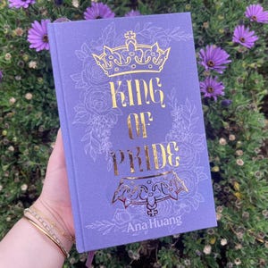 May include: A purple hardcover book with a gold crown and the title "King of Pride" by Ana Huang.