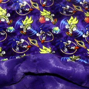 May include: Purple fleece blanket with a printed pattern of Sonic the Hedgehog and Super Sonic characters running through a galaxy background.
