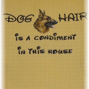May include: A yellow kitchen towel with black embroidered text that reads "Dog hair is a condiment in this house". A German Shepherd dog's head is embroidered above the text.