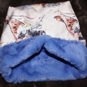 May include: A white and blue fabric neck warmer with a printed design of a wizard with a wand and a book. The neck warmer is lined with soft blue faux fur.