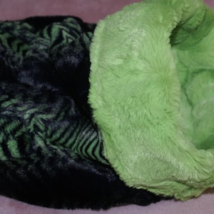 May include: A black and green faux fur neck warmer with a long, fluffy green lining. The neck warmer is made of soft, plush fabric.