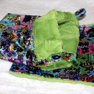 May include: A green plush pet bed with a colorful printed fabric lining featuring cartoon characters. The bed is folded in half, showing the inside lining.