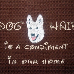 May include: A brown waffle weave kitchen towel with white embroidery that reads "Dog hair is a condiment in our home". A white dog silhouette is embroidered in the center of the towel.