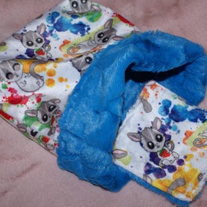 May include: A blue and white baby blanket with a colourful watercolour print of sugar gliders. The blanket has a soft, plush lining.